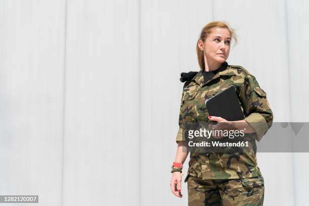 mature blond female army soldier holding digital tablet while looking away at military base on sunny day - army soldier photos et images de collection