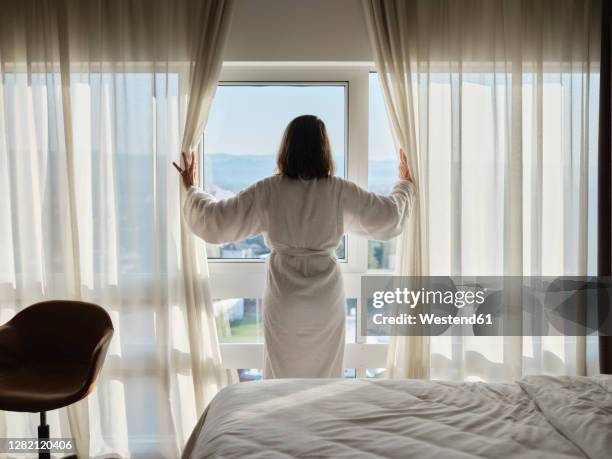 woman opening white curtain while looking through window at luxury hotel room - curtain hotel stock-fotos und bilder