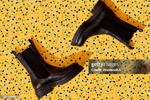 pair of black leather boots on yellow terrazzo pattern - bota de pele imagens e fotografias de stock