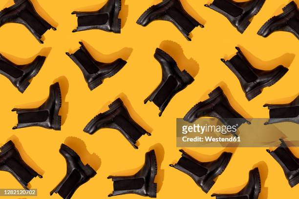 pattern of black leather boots against yellow background - black shoe stock-fotos und bilder