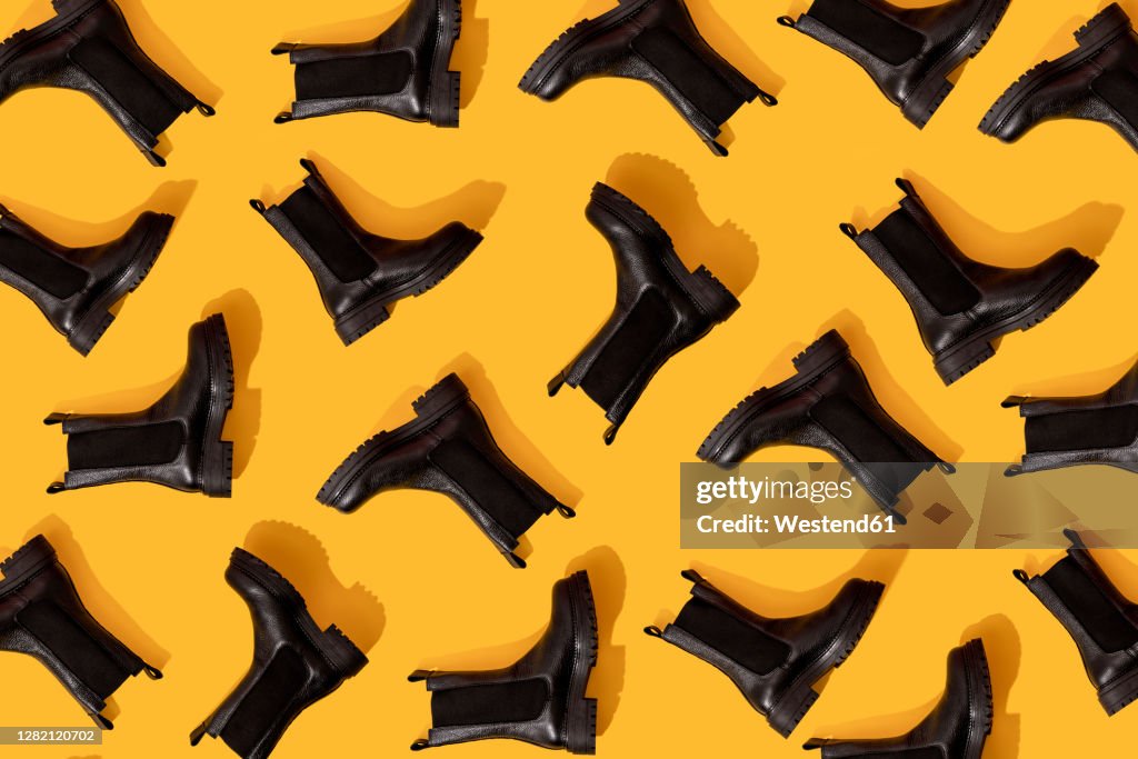 Pattern of black leather boots against yellow background