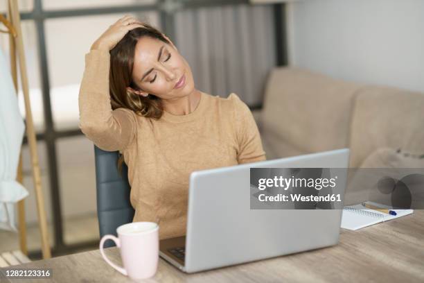 businesswoman doing neck exercise while working on laptop at home - neck stretch stock pictures, royalty-free photos & images