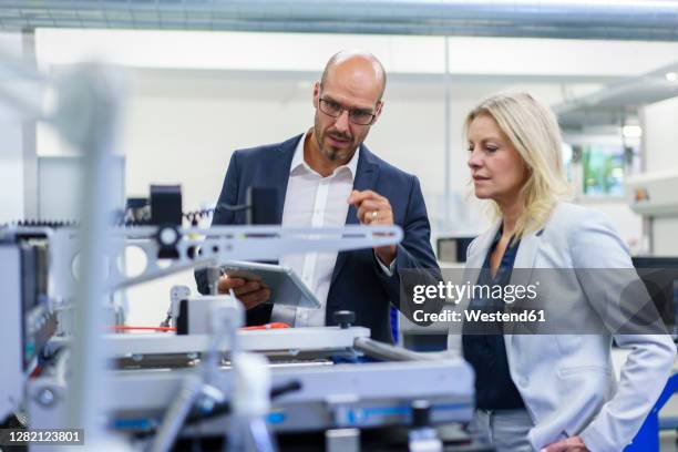 confident businessman and businesswoman discussing while looking at machinery in factory - 40 44 years blond hair mature man factory stock pictures, royalty-free photos & images