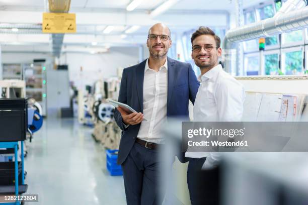 smiling male colleagues standing by machinery at illuminated factory - industrie porträt stock-fotos und bilder