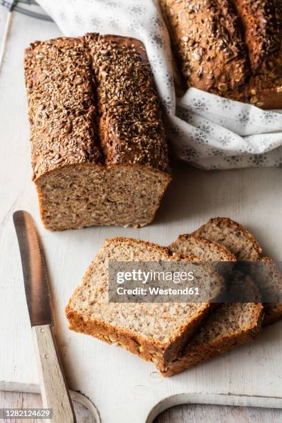 loaf and slices of brown bread on cutting board - vollkornbrot stock-fotos und bilder