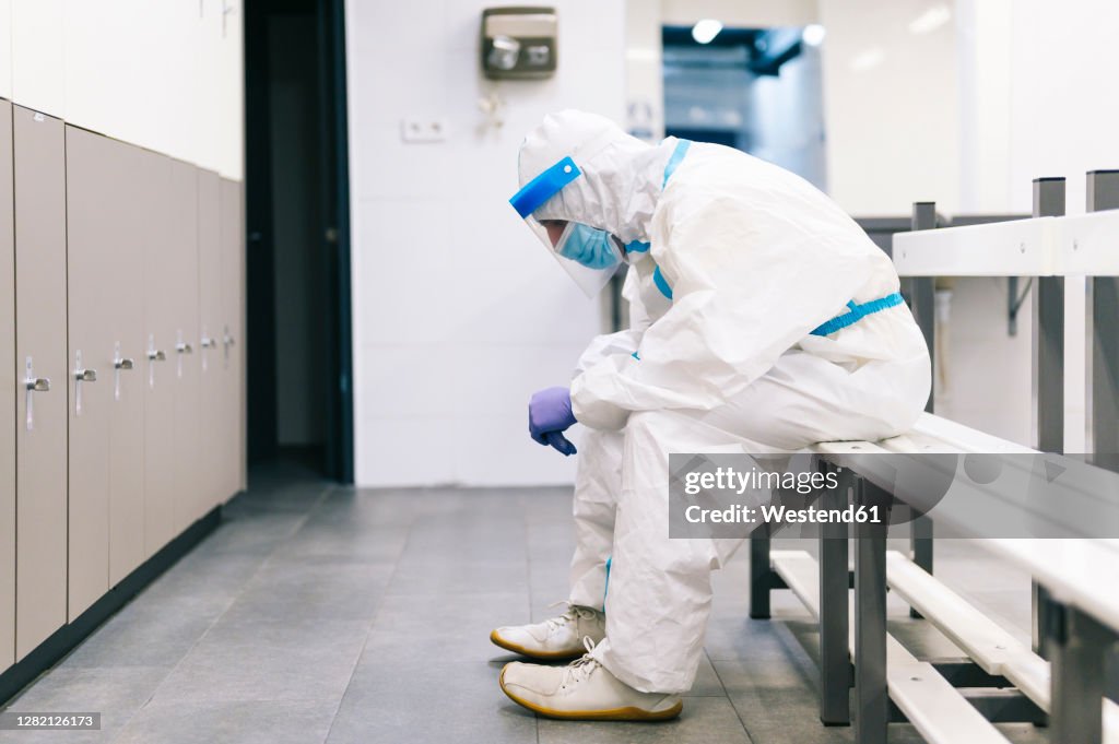 Thoughtful man wearing protective suit sitting on bench in hospital