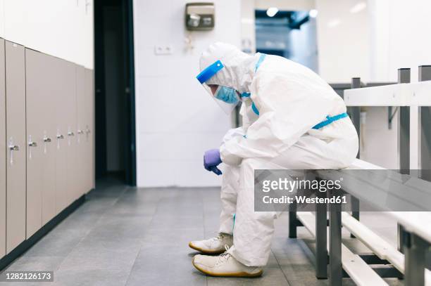 thoughtful man wearing protective suit sitting on bench in hospital - intensive care unit stock pictures, royalty-free photos & images