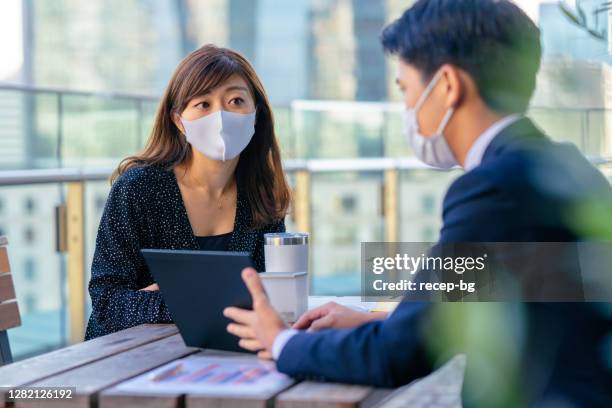 businessman and businesswoman having business meeting in outdoor café with protective face masks for illness prevention - business meeting with masks stock pictures, royalty-free photos & images