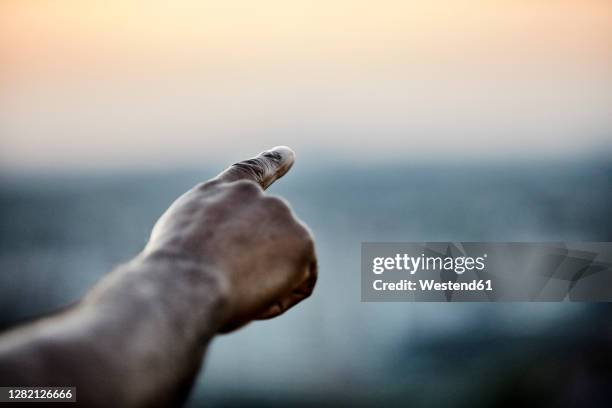 cropped hand of man pointing at sky from building terrace during sunset - finger pointing stock-fotos und bilder