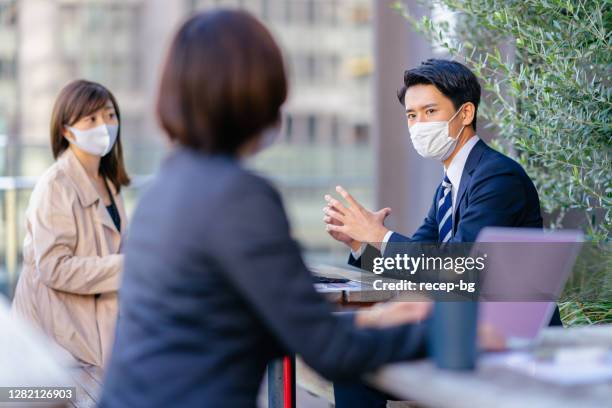 business people having business meeting in outdoor café with protective face masks for illness prevention - business meeting with masks stock pictures, royalty-free photos & images