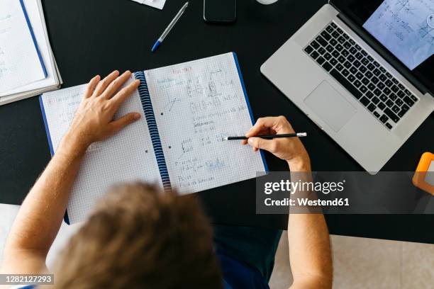male student solving mathematical equations in workbook while sitting at table - solving math stock pictures, royalty-free photos & images