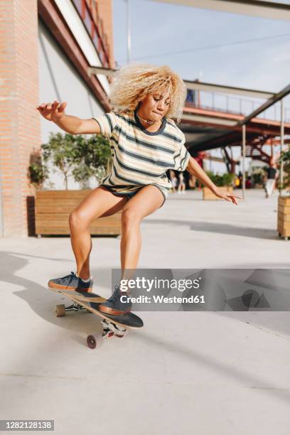 blond woman with arms outstretched skateboarding on footpath during sunny day - women skateboarding stock pictures, royalty-free photos & images