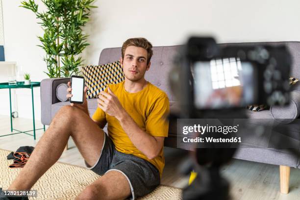 fitness trainer showing mobile phone to camera while sitting at home - male influencer stock pictures, royalty-free photos & images