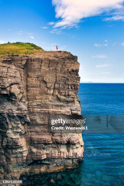 distant view of woman standing on cliff by sea against sky - russki insel im japanischen meer stock-fotos und bilder