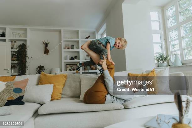 mother picking son on leg while playing on sofa at home - side lying leg lift stock pictures, royalty-free photos & images