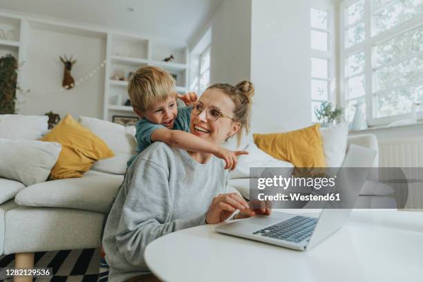 boy pointing at laptop while standing behind mother at home - geste de la main photos et images de collection