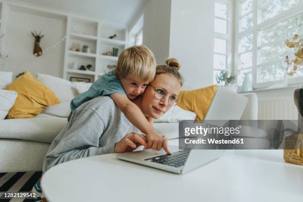 boy doing mischief on laptop while standing behind mother at home - working from home stock-fotos und bilder