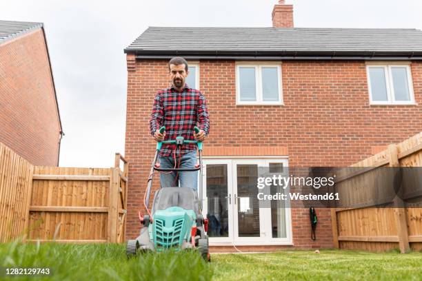 mid adult man using lawn mower for mowing at backyard - mowing stock pictures, royalty-free photos & images