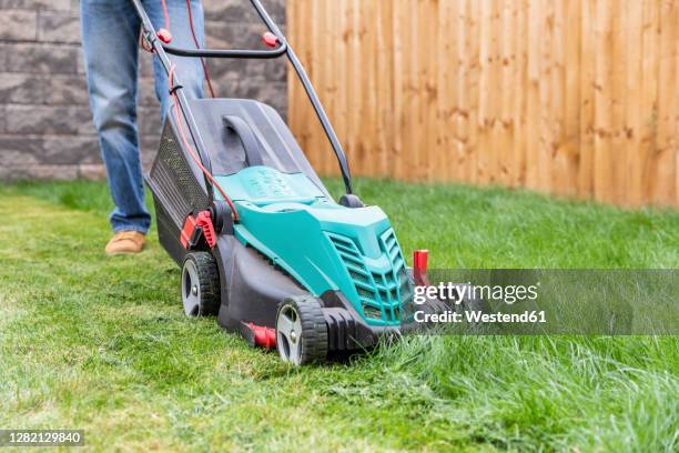 mid adult man standing with lawn mower at backyard - mowing stock pictures, royalty-free photos & images