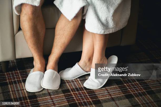 feet of a man and a woman in slippers close-up. a young couple in dressing gowns are sitting on a sofa or chair. - halb mann halb frau stock-fotos und bilder