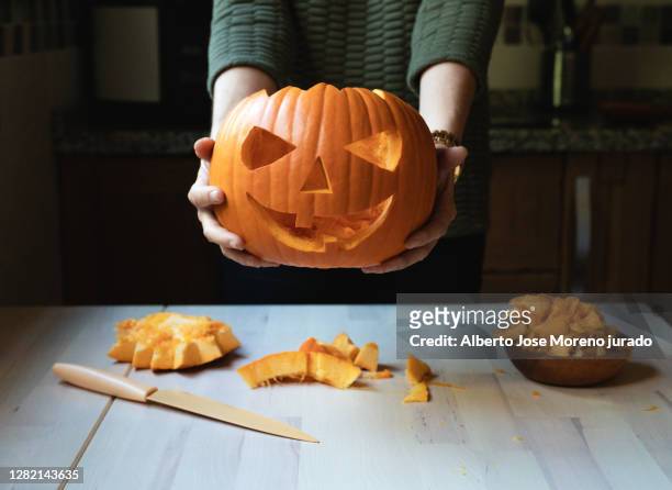 woman in front of a table holding a carved pumpkin on the occasion of halloween - jack o' lantern fotografías e imágenes de stock