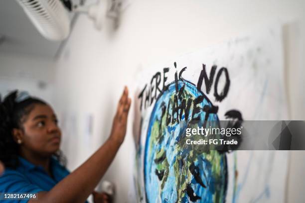 estudiante arreglando en la pared un cartel sobre cuestiones ambientales - no hay planeta b - social justice fotografías e imágenes de stock