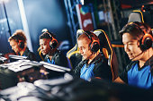 Team of four professional cybersport gamers wearing headphones participating in eSport tournament, playing online video games