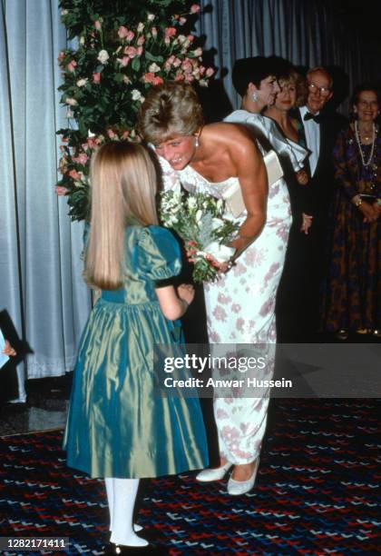 Diana, Princess Of Wales, wearing a ivory and pink silk crepe one sleeved evening dress designed by Catherine Walker, is presented with a bouquet by...