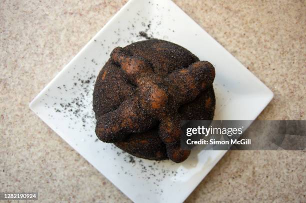 pan de muerto negro on a white plate on a stone kitchen benchtop - pan de muerto stockfoto's en -beelden