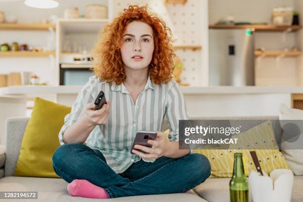 worried young woman is watching tv - young adult mobile phone serious stock pictures, royalty-free photos & images