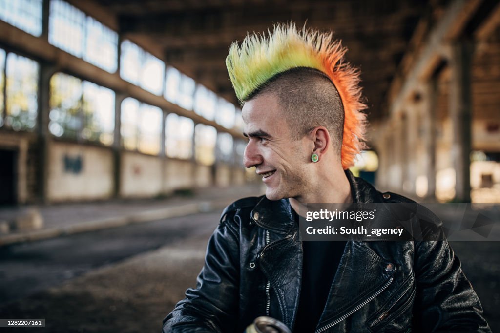 Panker with colorful coiffure sitting in abandoned warehouse and drinking beer