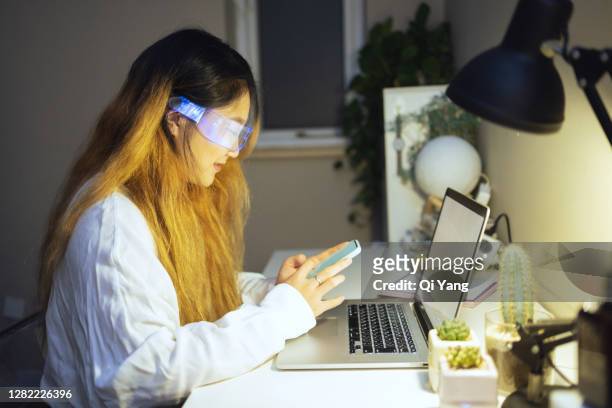 woman wearing augmented reality glasses using smartphone at home - smart glasses eyewear foto e immagini stock