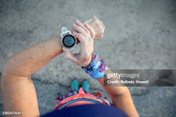 mature age runner prepares her smart watch for her run - run watch stock pictures, royalty-free photos & images