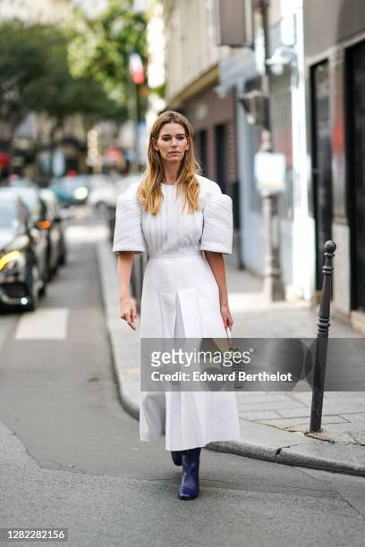 Natalia Verza wears a white pleated dress with puff shoulders, a white mesh woven leather bag, blue leather boots, outside Paco Rabanne, during Paris...