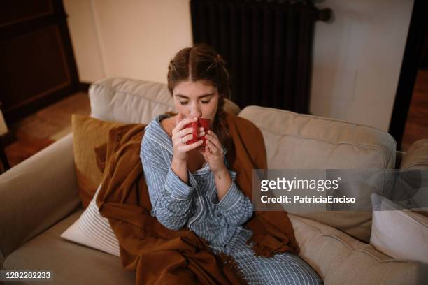 young woman with a cup sitting on a sofa - pyjamas stock pictures, royalty-free photos & images