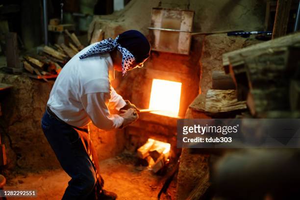 senior pottery craftsmen stoking the fire in his large kiln - pottery kiln stock pictures, royalty-free photos & images