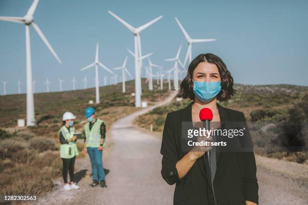 tv news reporter woman with face mask making reportage about a renewable energy during pandemic - journalist stock pictures, royalty-free photos & images