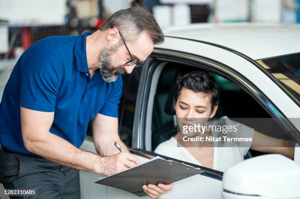 caucasian auto mechanic with female client looking at car checklist with bill at auto repair center. female client sitting in car. customer service, quality of service. - customer service documents foto e immagini stock