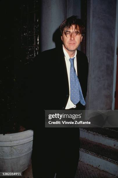 British singer-songwriter Bryan Ferry wearing a black suit over a white shirt and blue tie, his hands in his pockets, location unknown, circa 1990.