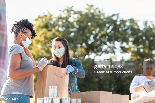 young women discuss contents of bag at food drive - charity and relief work stock pictures, royalty-free photos & images