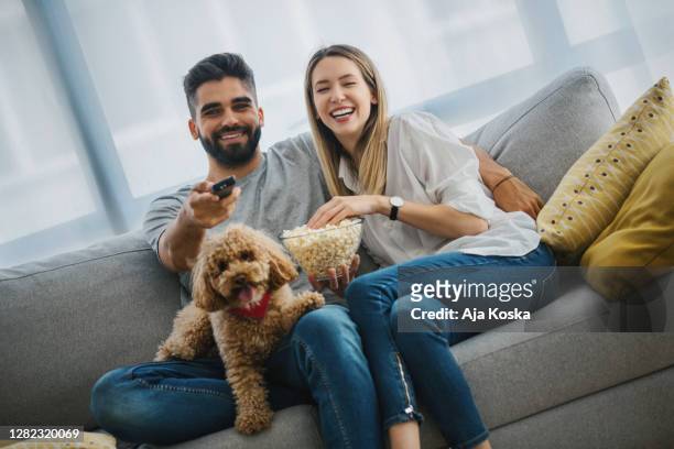 young couple laughing while watching their favorite series on tv. - young couple at movie together imagens e fotografias de stock