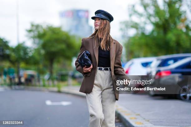 Sophia Roe wears a black leather beret hat, a brown oversized blazer jacket, a black top, a black leather Bottega Veneta bag, white flared long...