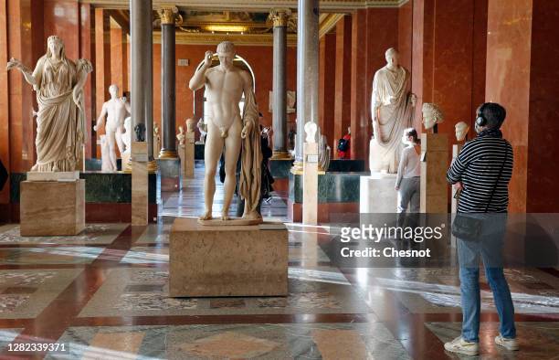 Visitor wearing a protective face mask looks at marble statues at the Louvre museum during the coronavirus pandemic on October 26, 2020 in Paris,...
