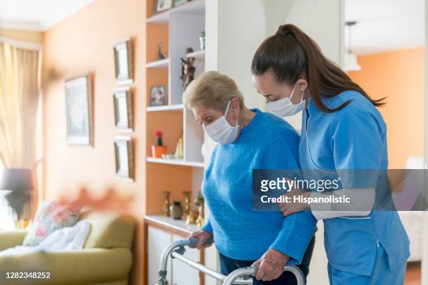 häuslichebetreuerträgt eine gesichtsmaske, während sie einer seniorin hilft, mit einem mobilitätswanderer zu gehen - care stock-fotos und bilder