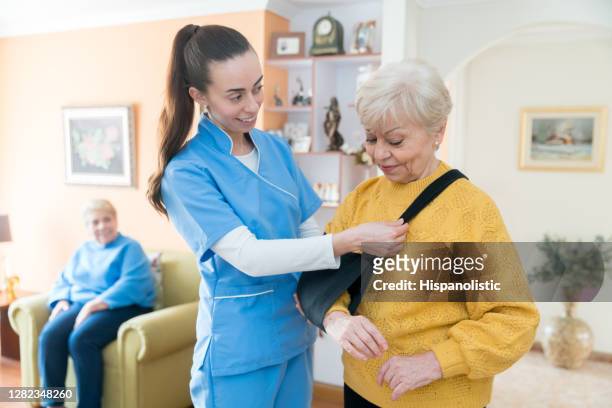 enfermera ayudando a una mujer de último año a poner un cabestrillo de brazo en una casa de retiro - cabestrillo de brazo fotografías e imágenes de stock