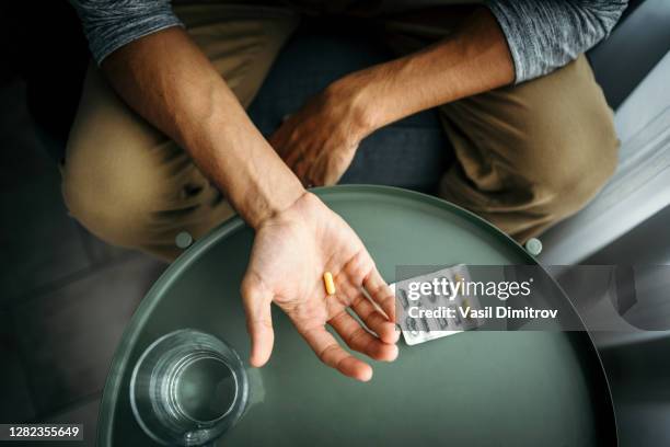 young man holding a pill in his hand in front of a table with glass of water. medical treatment / drug use concept. - antidepressivo imagens e fotografias de stock