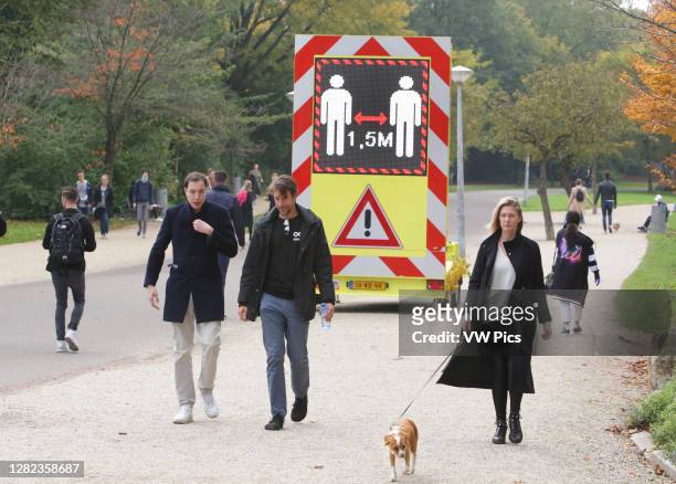 People walks past near a electronic sign urging people to practice social distancing and keep 1.5 meters at the Vondelpark amid the Coronavirus...