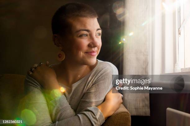 a young woman in her living room hugging herself in the sunlight - seitenblick stock-fotos und bilder