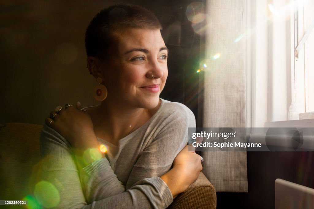 A young woman in her living room hugging herself in the sunlight
