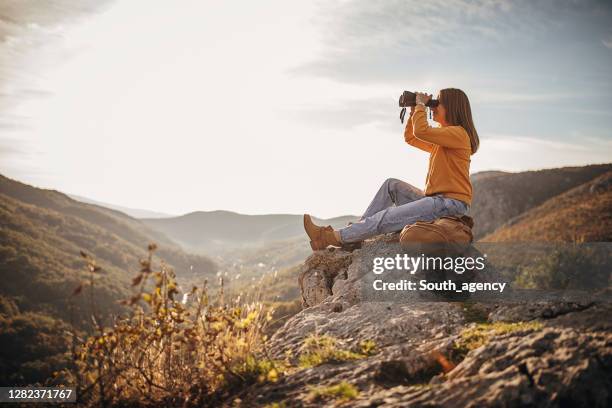 de zitting van de vrouw met verrekijkers op bergpiek in zonsondergang - verrekijker stockfoto's en -beelden